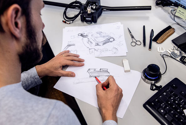 Designer skizziert Produktkonzepte an einem Schreibtisch mit Werkzeugen und Computerausrüstung.