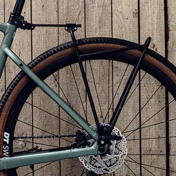 Nahaufnahme eines Fahrradhinterrads und einer Scheibenbremse mit einem montierten Fahrradträgerrahmen vor einem hölzernen Wandhintergrund