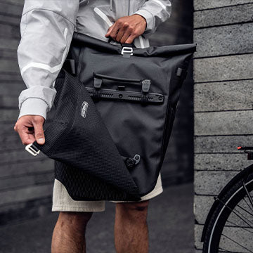 Eine Person hält einen schwarze ORTLIEB Vario in der Hand und demonstriert, wie einfach es ist, diesen in eine Fahrradtasche umzuwandeln.